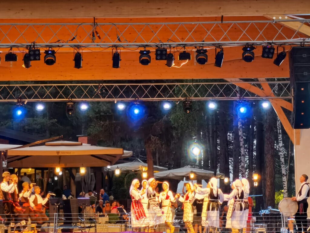 Traditional Serbian folk dance performance on a stage lit by blue and yellow lights.