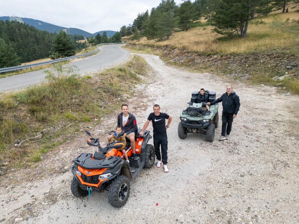 Family riding quads on a mountain road in Zlatibor with pine trees and winding road