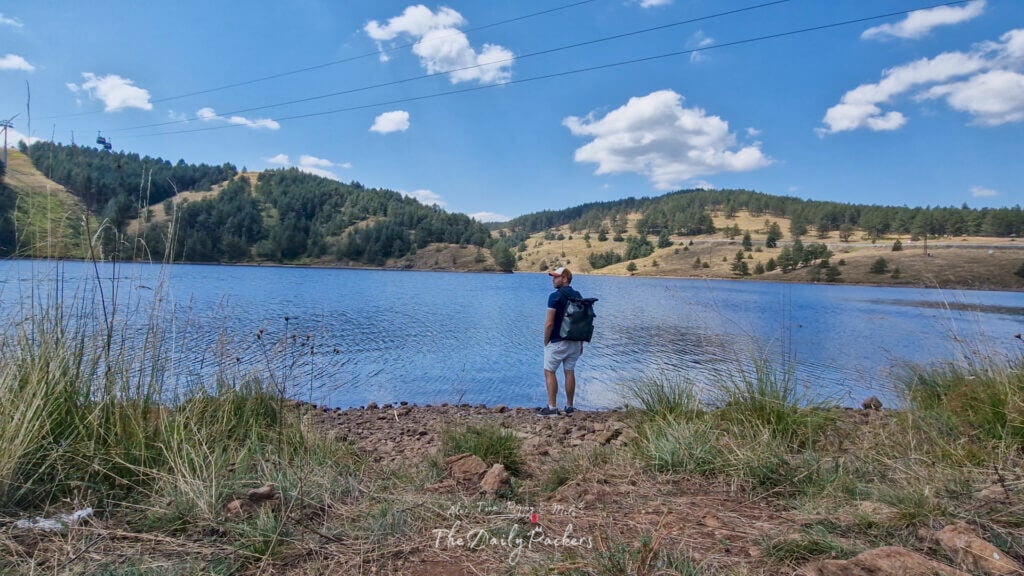 Man standing on the shore of Ribnica Lake surrounded by pine-covered hills