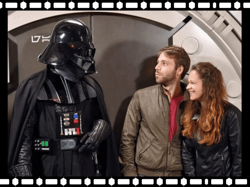 Couple souriant et posant à côté d'une personne en costume de Dark Vador dans un décor de science-fiction.
