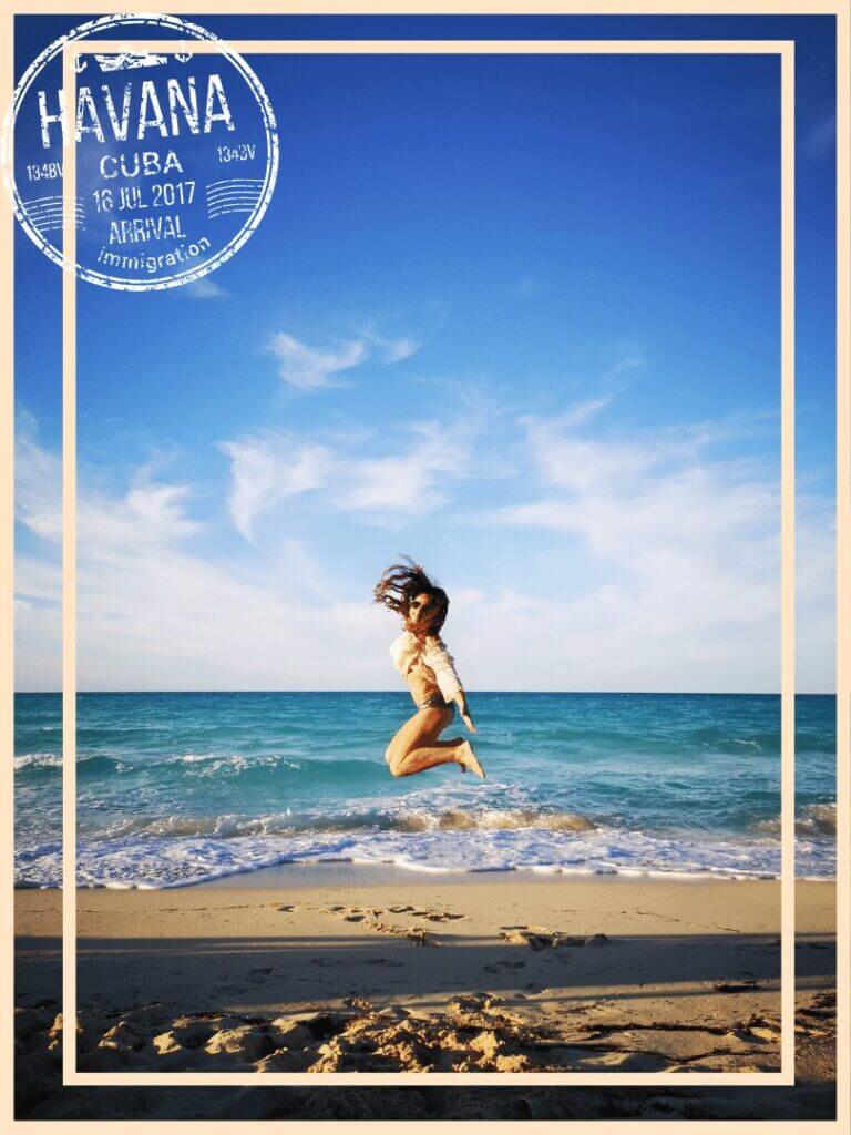 Femme sautant joyeusement sur une plage de sable à Cuba avec des vagues turquoise et un ciel bleu clair, encadrée par un timbre d'arrivée de La Havane.