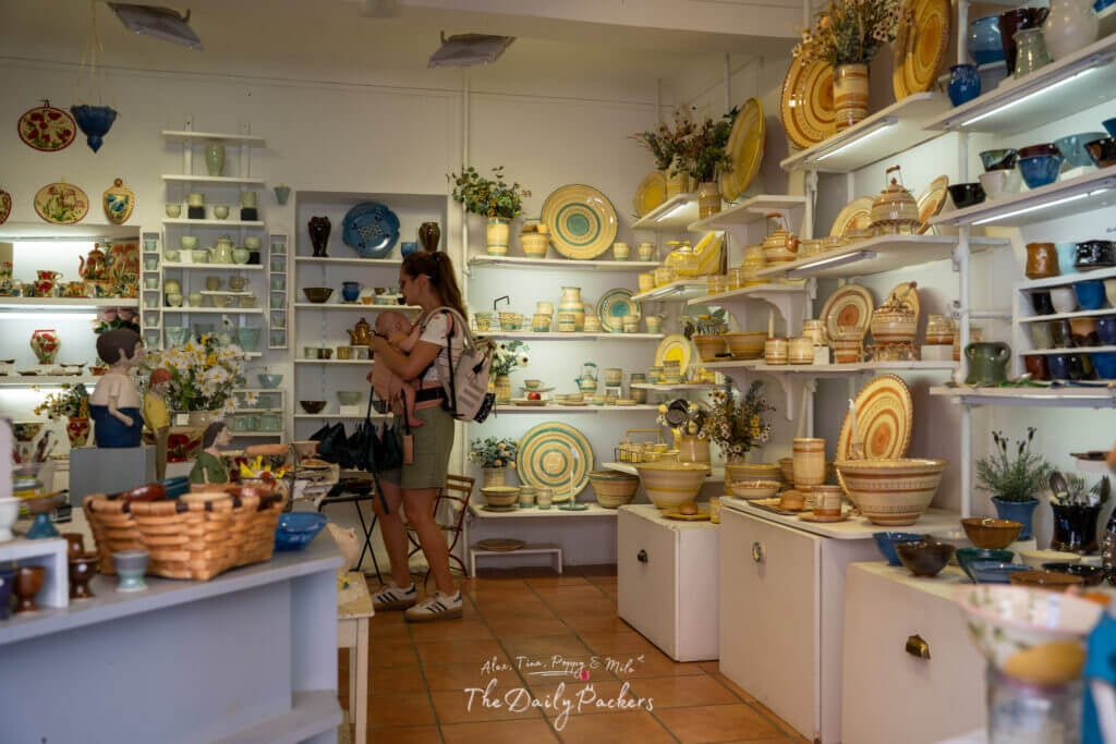 Femme avec un porte-bébé explorant une boutique de poterie colorée remplie de pièces en céramique faites à la main à Roussillon.