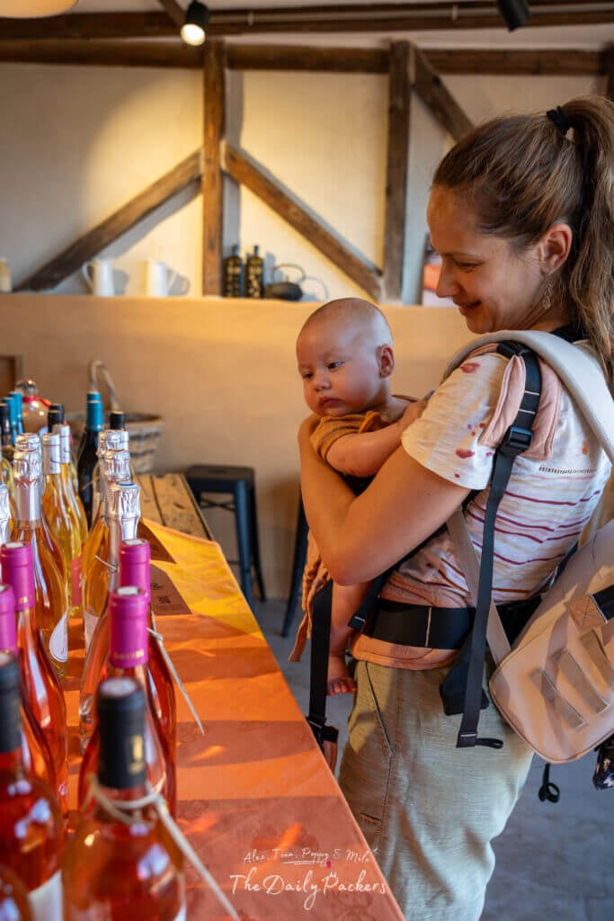 Femme tenant son bébé et regardant une rangée de bouteilles de vin rosé dans un magasin de vin rustique du Roussillon.