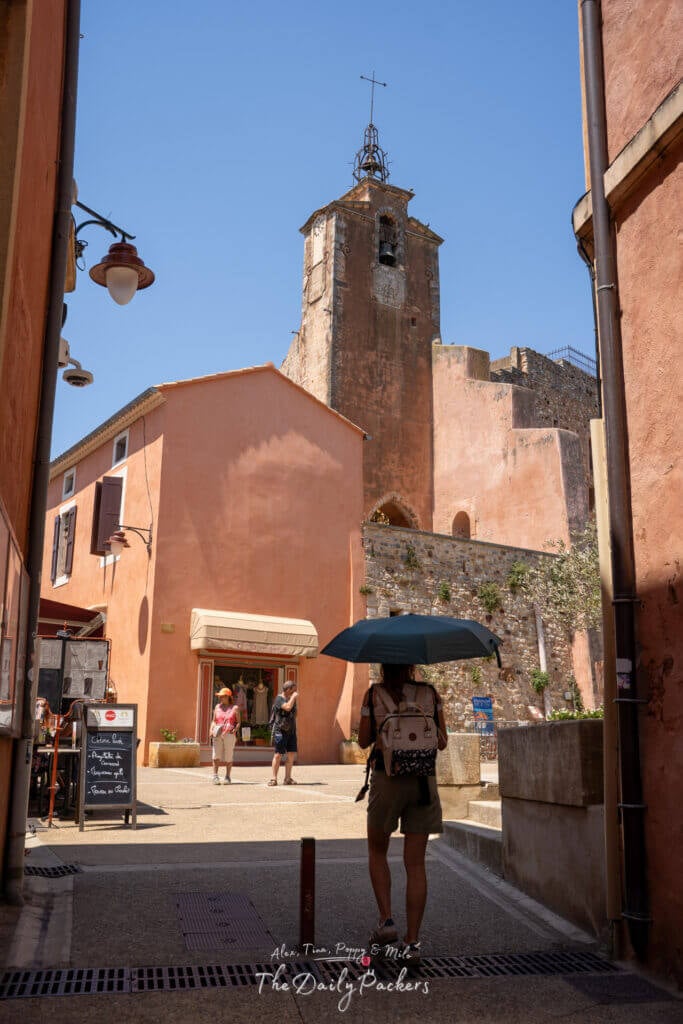 Ruelle de Roussillon bordée de maisons ocre avec un clocher en arrière-plan.