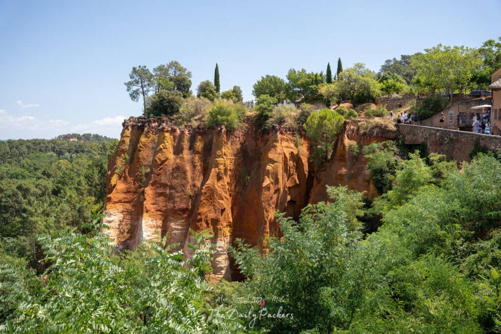 Des falaises ocre emblématiques entourées de verdure sous un ciel bleu éclatant en Roussillon.