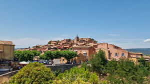 Panoramic view of Roussillon village, its ochre-colored houses clustered on the hilltop under a bright blue sky.