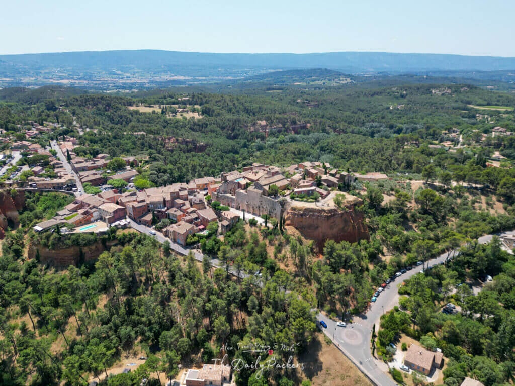 Vue aérienne de Roussillon entouré de forêts, montrant le village perché de façon spectaculaire sur des falaises ocres.
