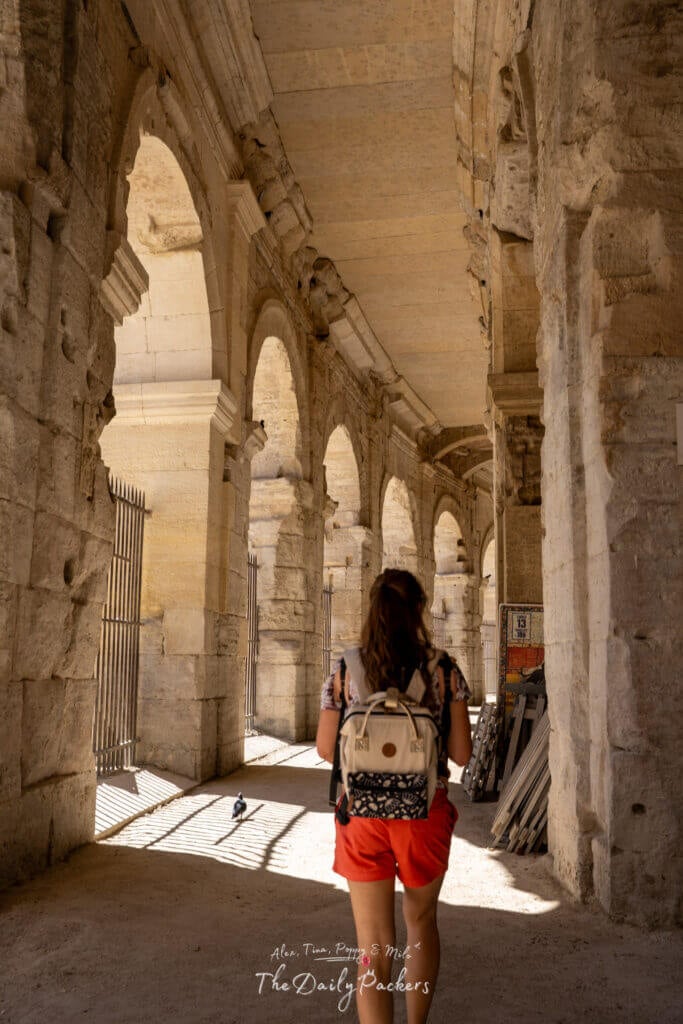 Femme marchant sous les arches de pierre de l'amphithéâtre d'Arles, à la lumière du soleil.