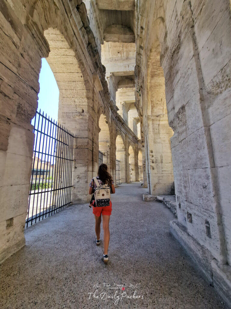Vue des arches intérieures de l'amphithéâtre d'Arles, la lumière du soleil projetant des ombres fortes sur les murs de pierre.