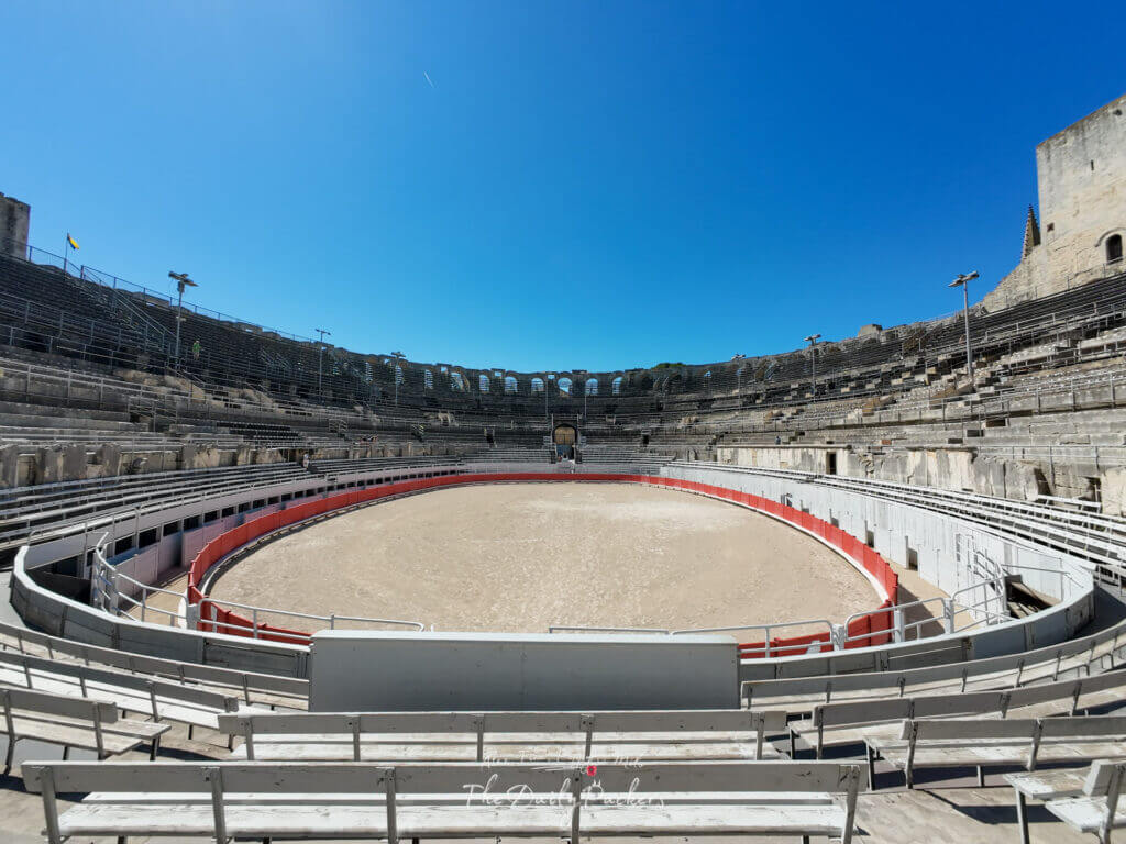Vue large de l'arène de l'amphithéâtre d'Arles montrant les rangées de sièges en pierre et l'anneau de spectacle en sable.