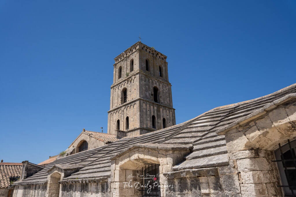 Clocher du Cloître Saint-Trophime s'élevant au-dessus des vieux toits de tuiles sous un ciel bleu éclatant.