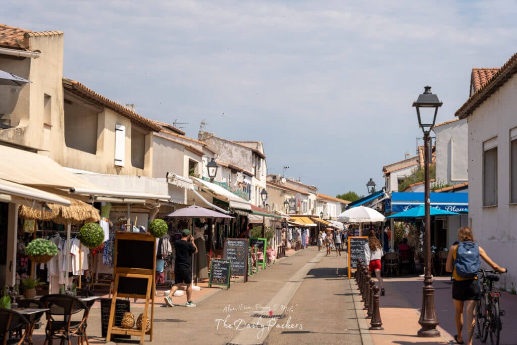 Rue principale des Saintes-Maries-de-la-Mer bordée de cafés, de boutiques et d'auvents colorés.