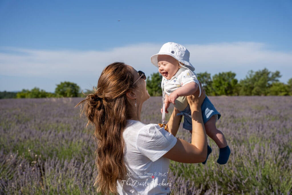 Femme soulevant un bébé en l'air en souriant, entourée de champs de lavande violette.