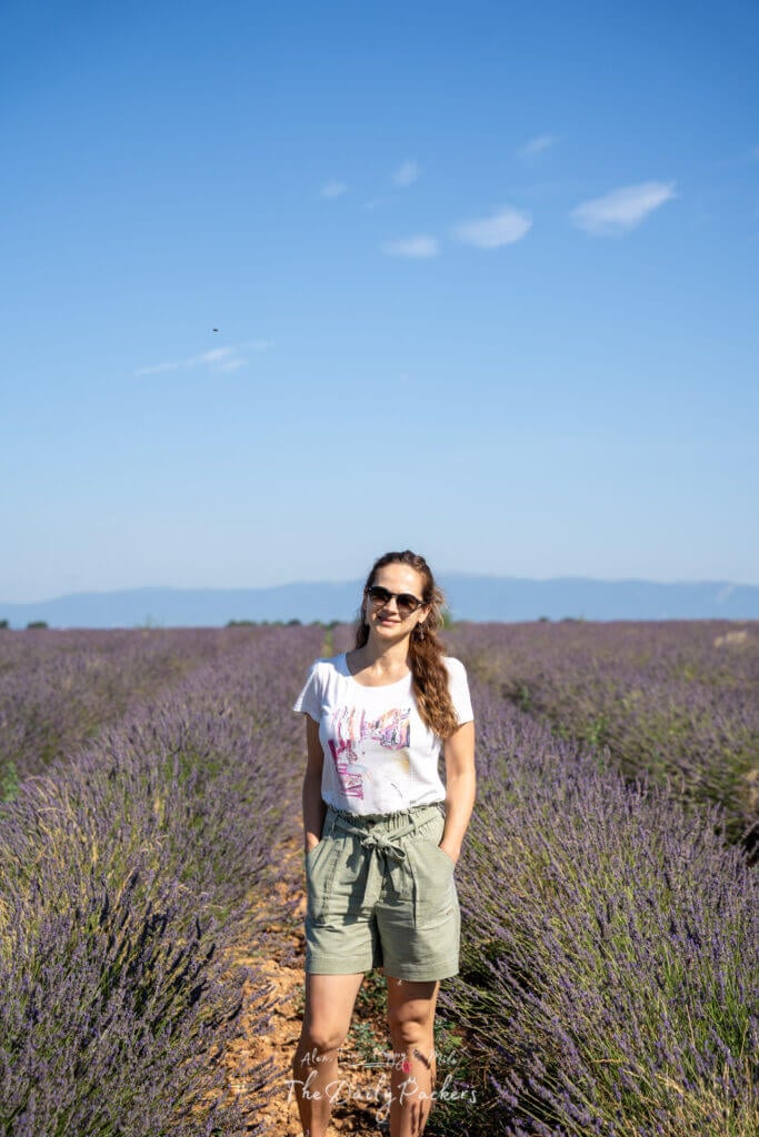 Femme se tenant avec assurance entre des rangées de lavande, souriant sous le soleil provençal.