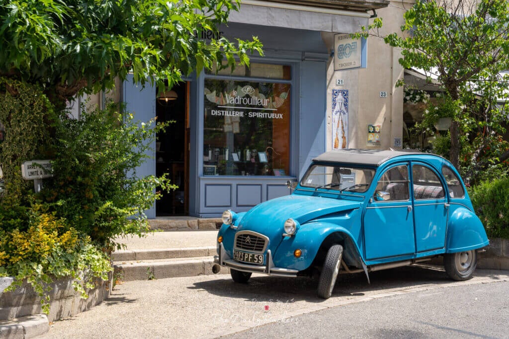 Citroën 2CV vintage bleu vif garée devant la boutique d'une distillerie locale dans un village provençal