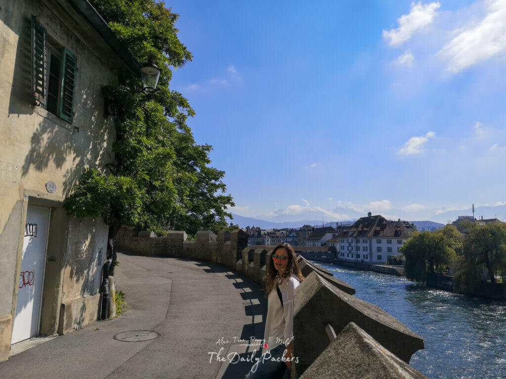 Woman leaning on the old rampart wall in Lucerne with views over the river, rooftops, and distant mountains on a sunny day.