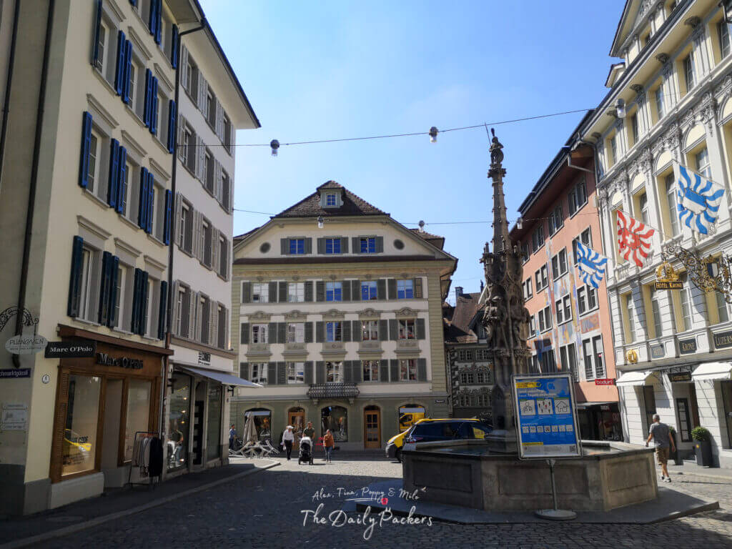 Charming street in Lucerne’s old town with cobbled pavement, fountain, and colorful historic buildings under sunny skies.