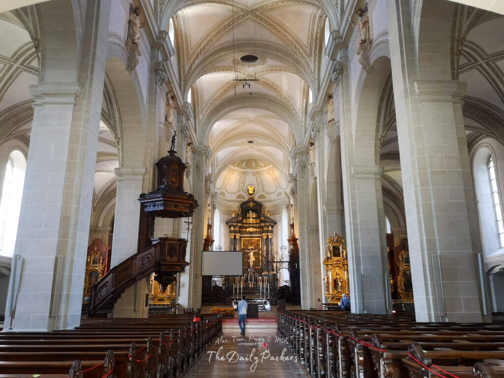 Inside Lucerne’s Hofkirche St. Leodegar with ornate baroque altar, tall arches, and detailed wooden pulpit.