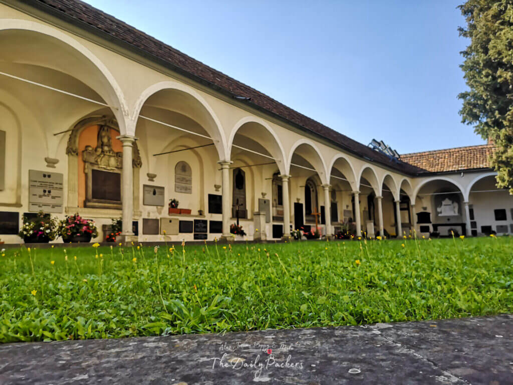 Hofkirche St. Leodegar’s peaceful cemetery with white arches, gravestones, flowers, and green lawn in Lucerne.