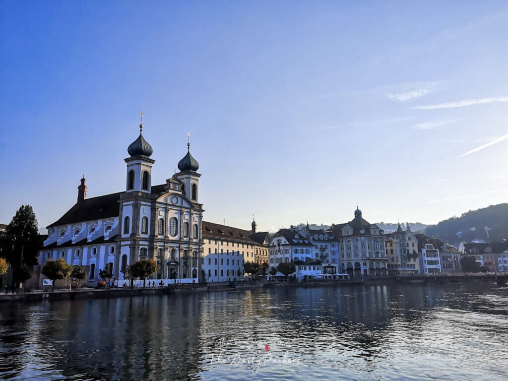 Lucerne’s Jesuit Church and historic buildings reflecting in the calm Reuss River during early evening light.