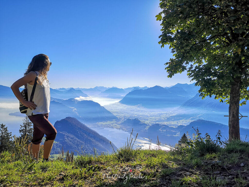 Woman with backpack admiring panoramic view over Lucerne and the Alps from Mount Pilatus, clear blue sky and distant peaks.