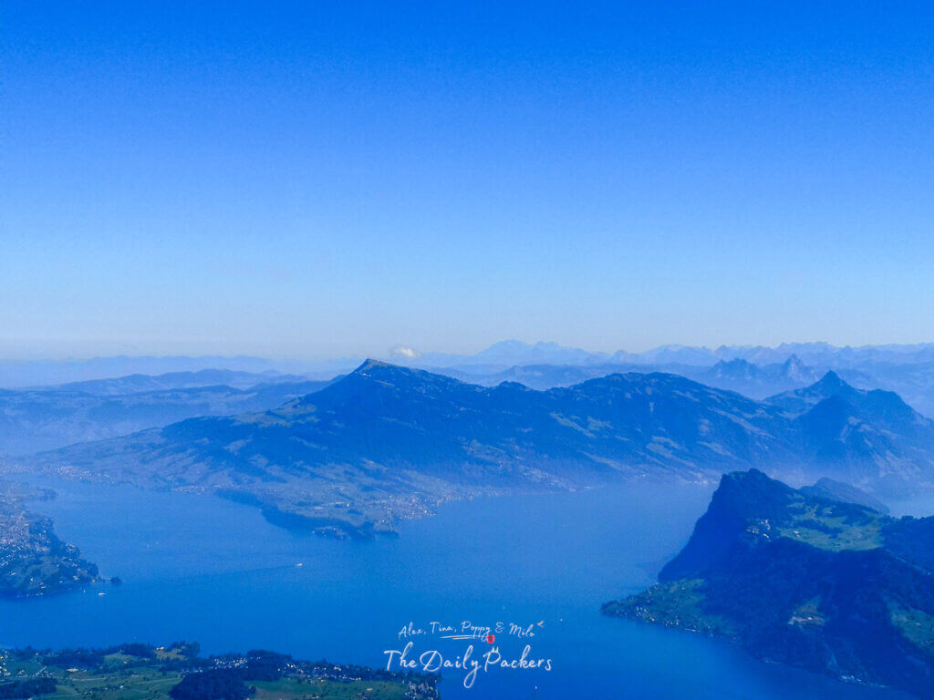 Expansive view over Lake Lucerne surrounded by hazy blue mountain ranges and clear skies from Pilatus summit.