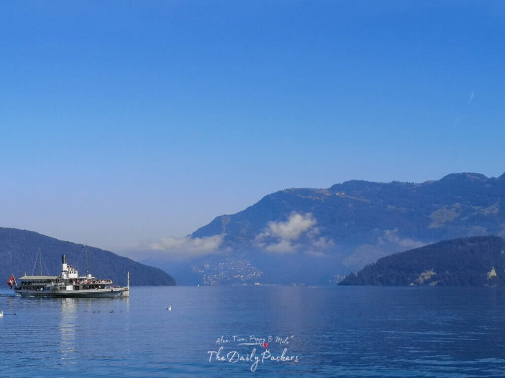 historic paddle steamer cruising on Lake Lucerne with forested hills and alpine peaks in the background on a sunny day