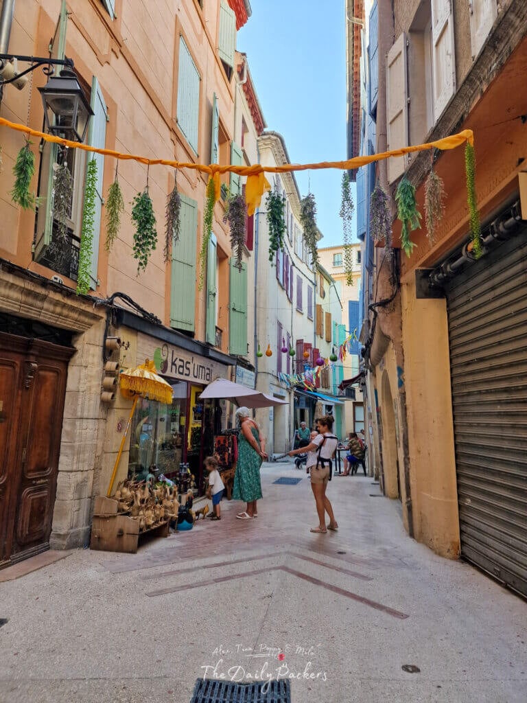Charming alley in Manosque with pastel-colored shutters and hanging greenery between the buildings.