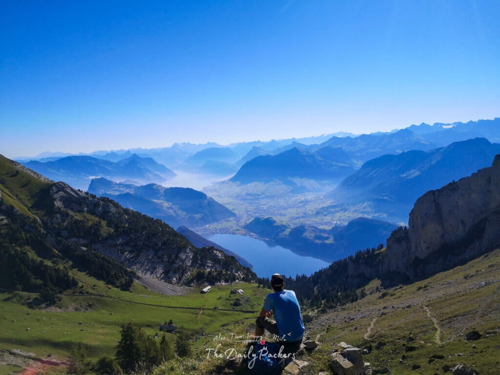Homme assis seul sur un rocher contemplant une superbe vallée alpine et le lac des Quatre-Cantons depuis le mont Pilate.