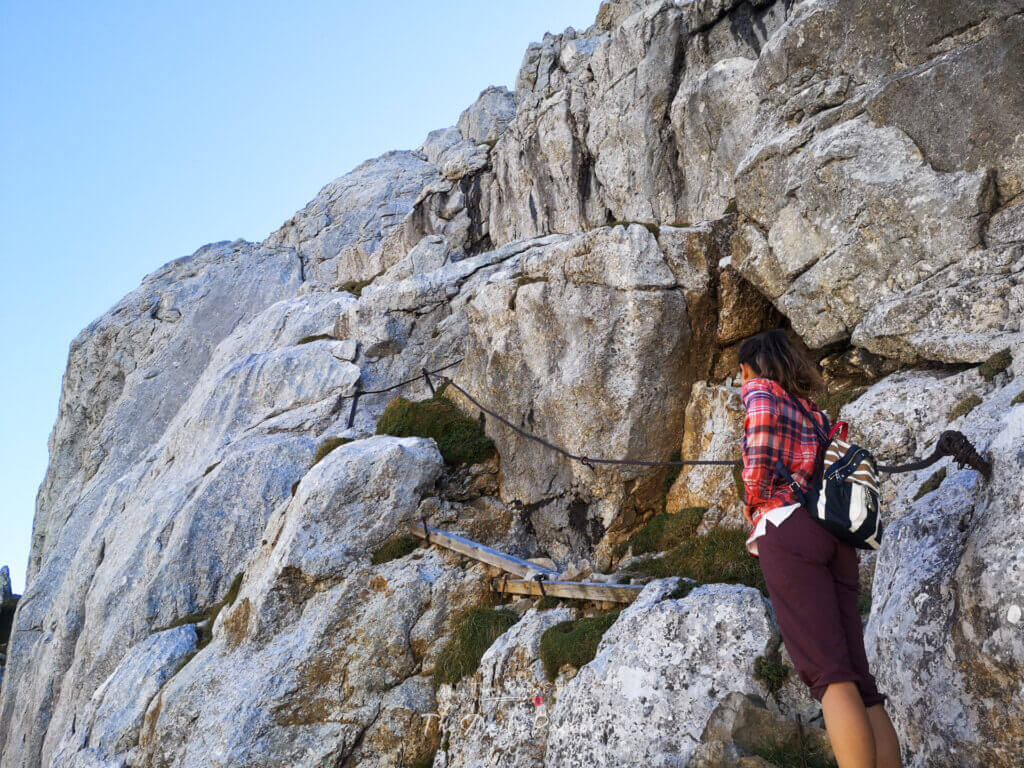 Femme escaladant une section rocheuse du sentier Matthorn sur le Mont Pilatus avec des chaînes pour se soutenir.