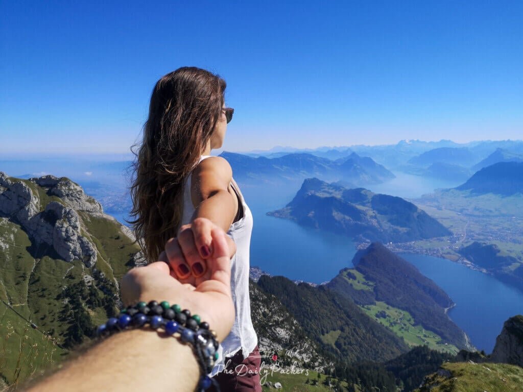 Homme tenant la main d'une femme au-dessus du lac des Quatre-Cantons avec des vues panoramiques et des bleus alpins profonds en arrière-plan.