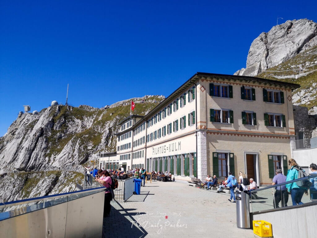 Bâtiment principal de la station du Mont Pilatus avec des touristes profitant du soleil et de l'environnement montagneux impressionnant.
