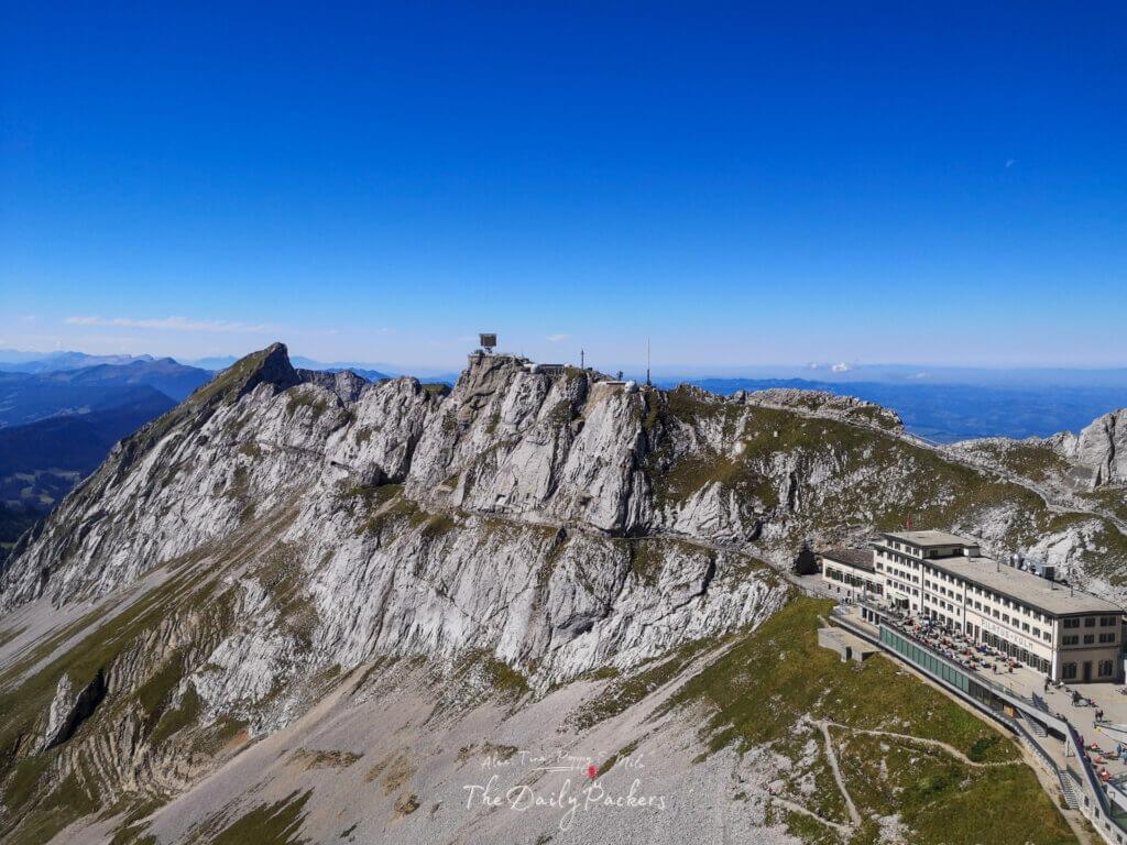 Le point de vue d'Esel et la station du Mont Pilatus vus depuis la crête opposée, encadrés par des pics calcaires escarpés.