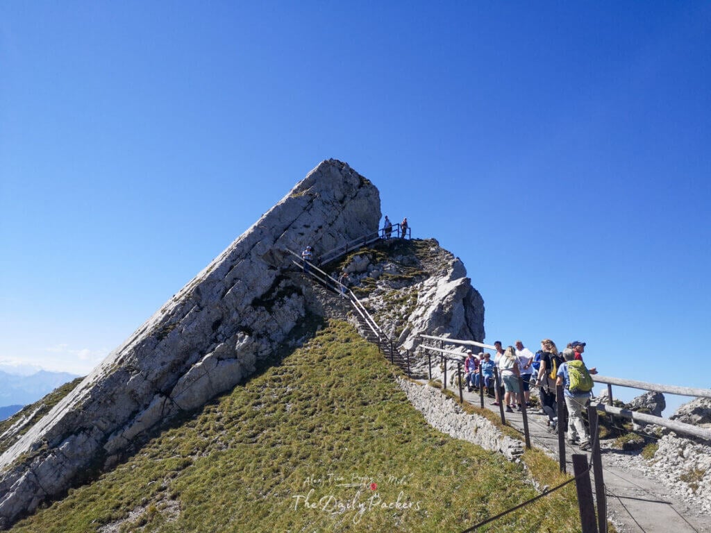 Groupe de randonneurs remontant le sentier d'observation du sentier des fleurs sur le mont Pilatus, sous un ciel d'été d'un bleu éclatant.