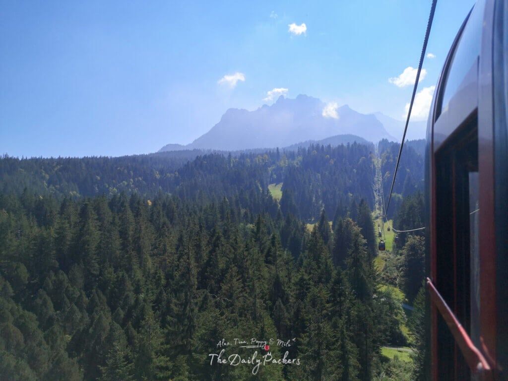 Trajet en téléphérique à travers une forêt dense avec une vue brumeuse sur les sommets du Mont Pilatus en arrière-plan par une journée ensoleillée.