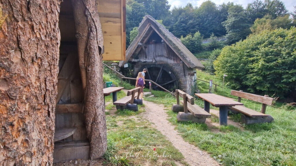Couple s'approchant d'un moulin à eau rustique situé parmi des bancs de pique-nique et de la verdure lors d'une randonnée paisible.