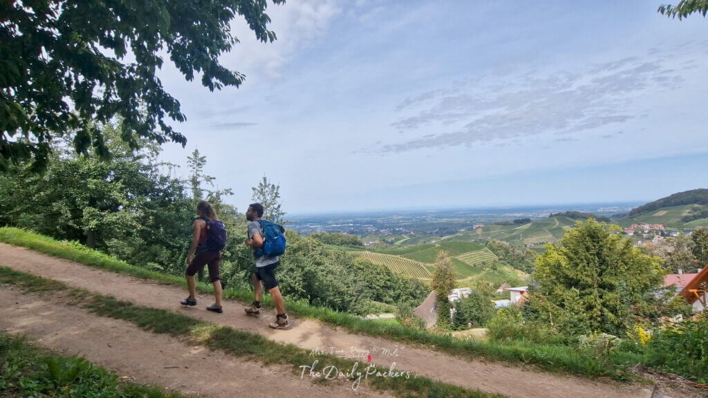 Des randonneurs montent un sentier surplombant les vignobles et le village en contrebas, avec des vues panoramiques à l'horizon.