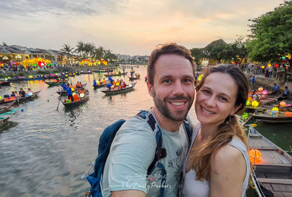 The Daily Packers, Alex & Tina smiling in Hoi An during sunset with traditional boats in the background