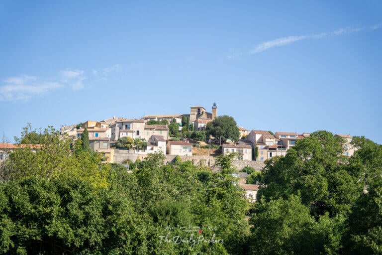 Distant view of Valensole village perched on a hilltop, surrounded by lush greenery with the church tower standing out against a clear blue sky.