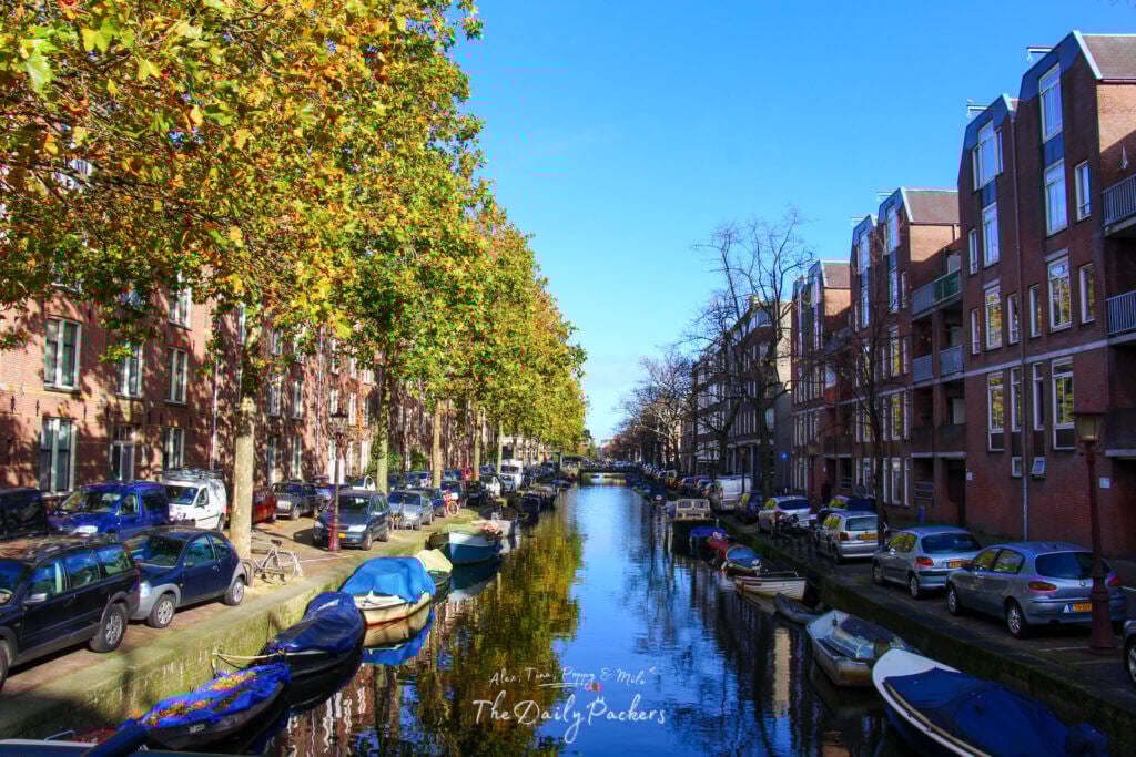 Bright and sunny canal scene in Amsterdam with autumn leaves and moored boats.