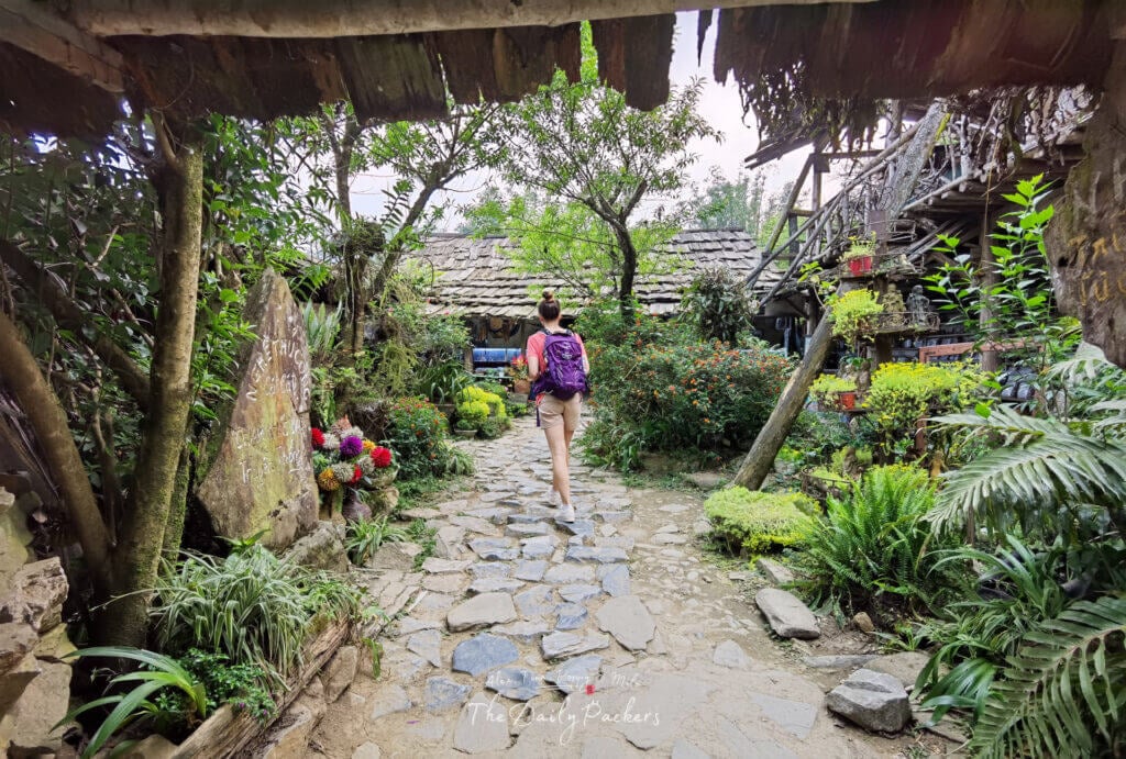 Woman walking into a charming stone courtyard filled with lush plants and flowers in Cat Cat Village