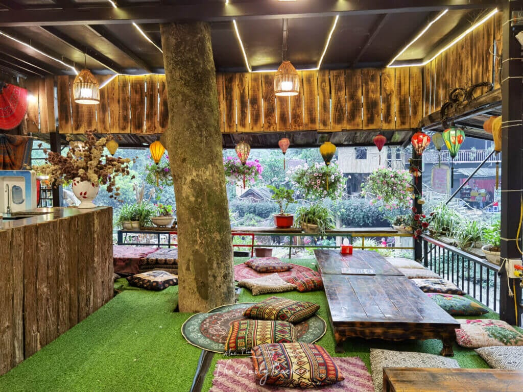 Cozy wooden restaurant in Cat Cat Village with low tables, colorful cushions, and hanging lanterns.