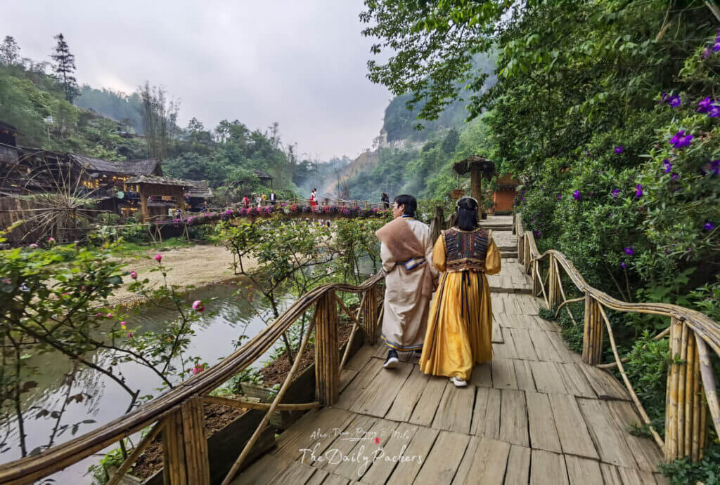 Couple in traditional ethnic clothing walking along a bamboo bridge path in Cat Cat Village.