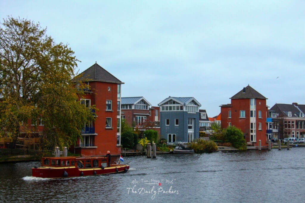 A classic canal in Haarlem with a vintage boat cruising past colorful modern buildings on a cloudy day.