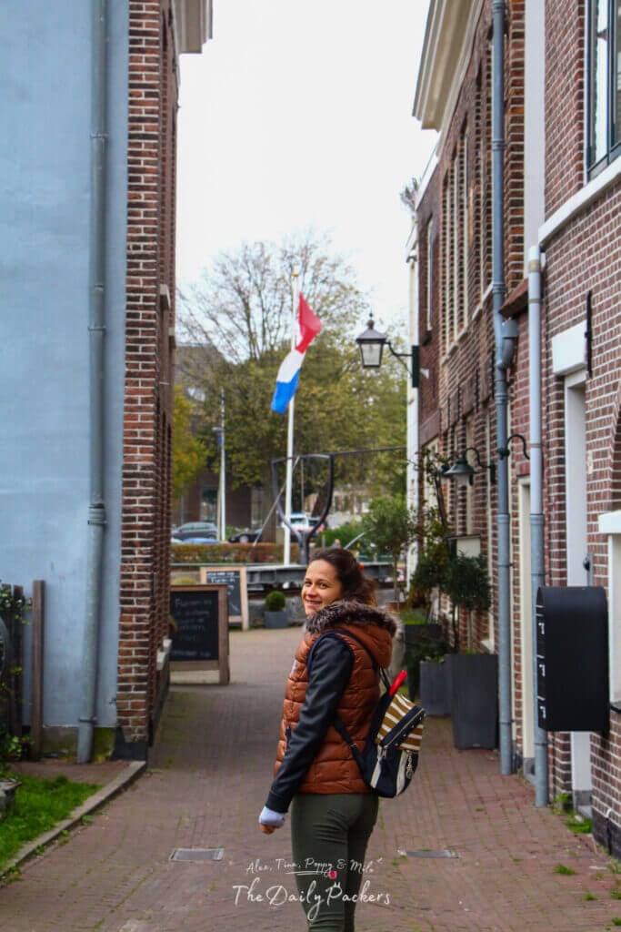 A woman smiling while walking through a narrow alley in Haarlem, with a Dutch flag waving in the background.