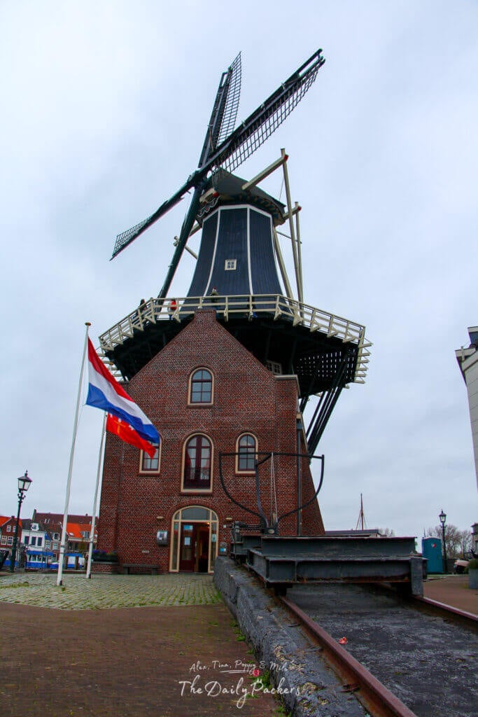 The full view of Molen de Adriaan windmill by the water in Haarlem, captured from across the canal under a grey sky.