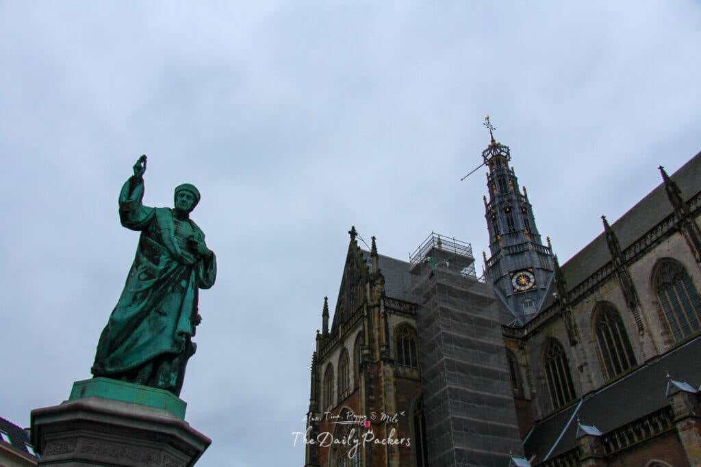 Statue in front of the Grote Kerk in Haarlem, with the church tower under renovation on a cloudy day