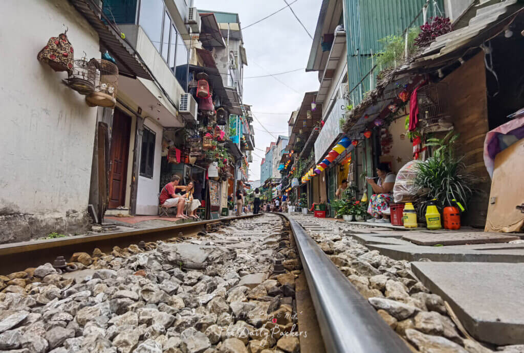 Vue en contre-plongée le long de la voie ferrée de la rue du train de Hanoi, avec des cages à oiseaux suspendues et des décorations colorées.