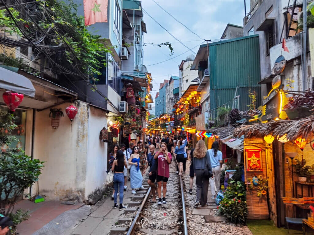 La rue du train de Hanoï en début de soirée, bondée de visiteurs se promenant entre les cafés et les lanternes lumineuses.