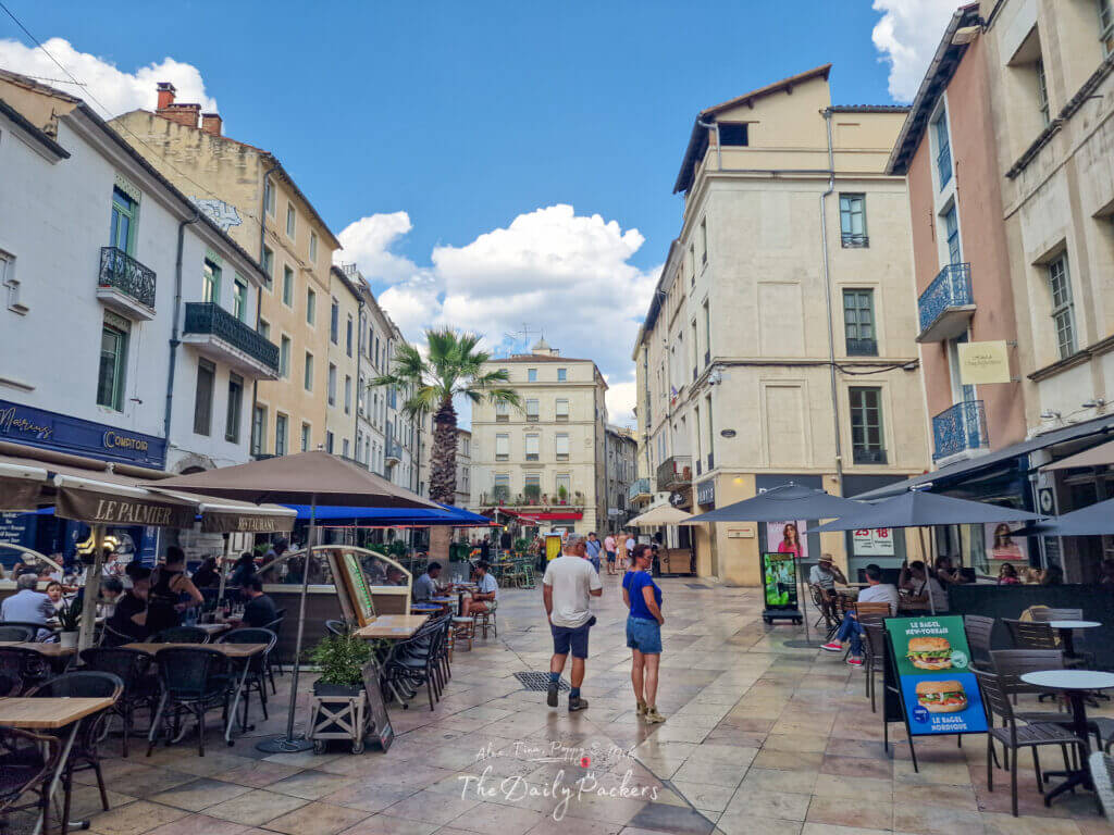 Rue piétonne animée de Nîmes, remplie de cafés, de gens qui dînent en plein air et d'une ambiance estivale décontractée.
